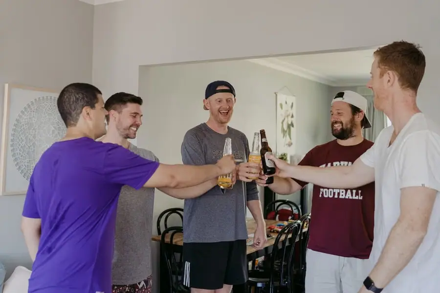 Five men clinking bottled drinks together in a sitting room