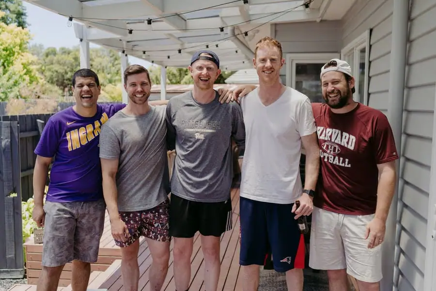 Five men posing together in casual clothes on a verandah