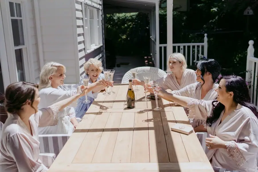 Women raising champagne glasses around a wooden outdoor table
