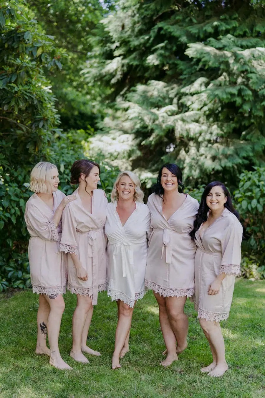 Bride and four friends posing together in pale robes beneath trees