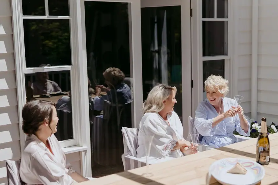 Women chatting and laughing with drinks at a sunny outdoor table