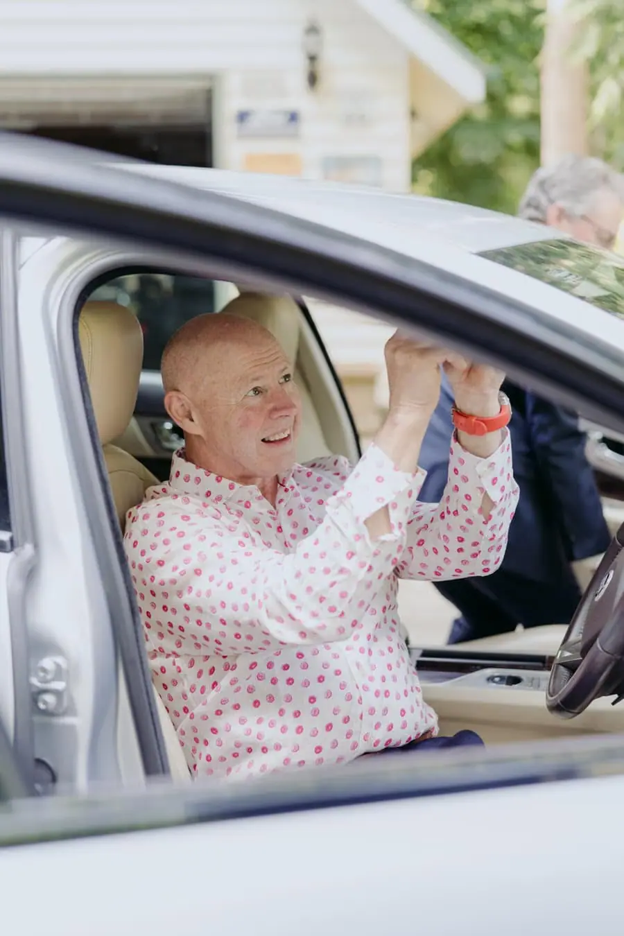 Man smiling from the driver's seat of a car with one hand raised
