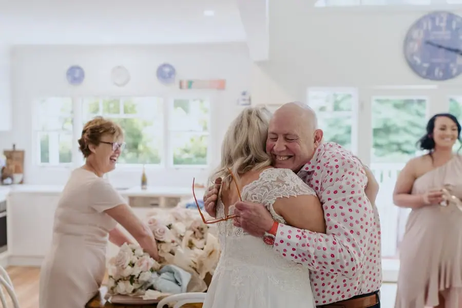 Bride embracing a smiling man as friends watch nearby