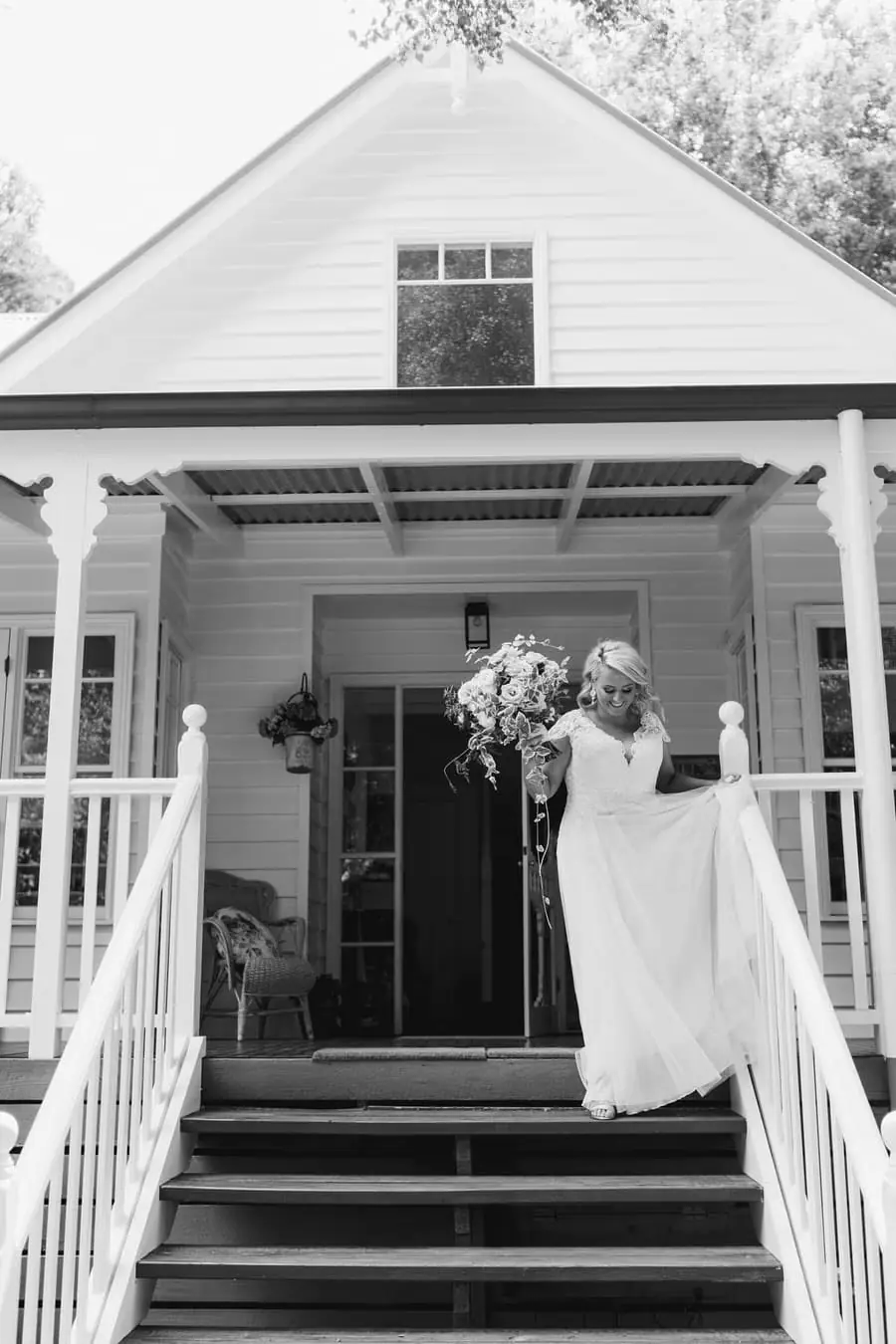Black-and-white photograph of the bride standing on house steps with her bouquet