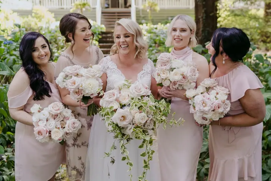 Bride and bridesmaids laughing together with white and pink bouquets