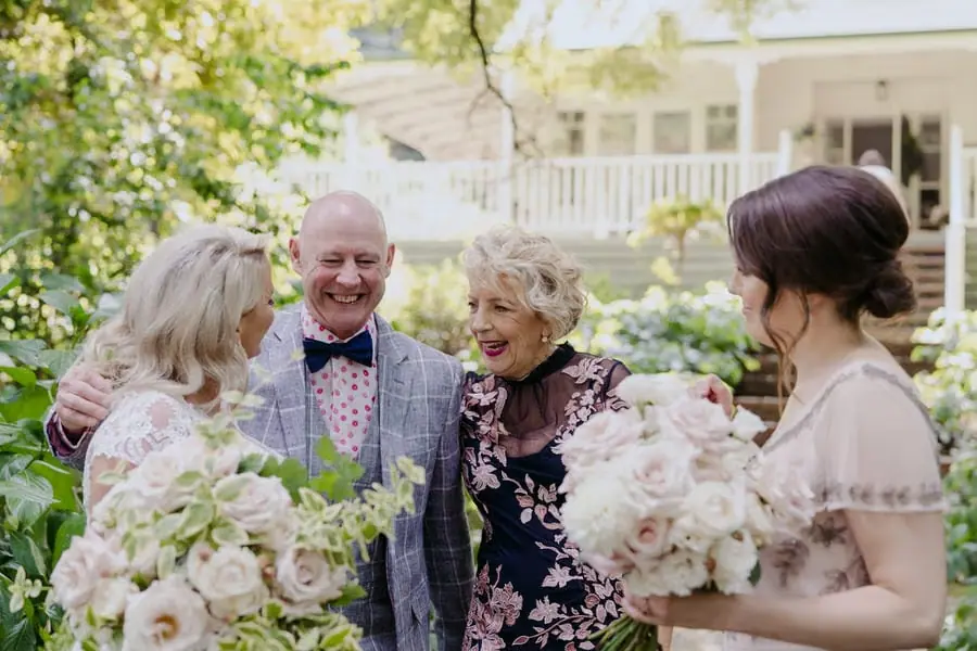 Bride chatting with smiling guests beneath garden trees