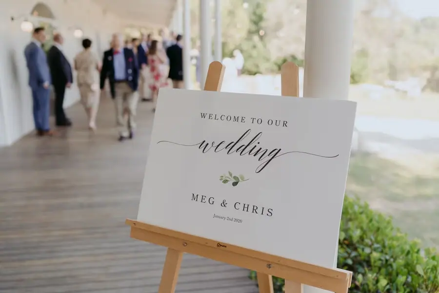 Wedding welcome sign displayed on a wooden easel beside a verandah