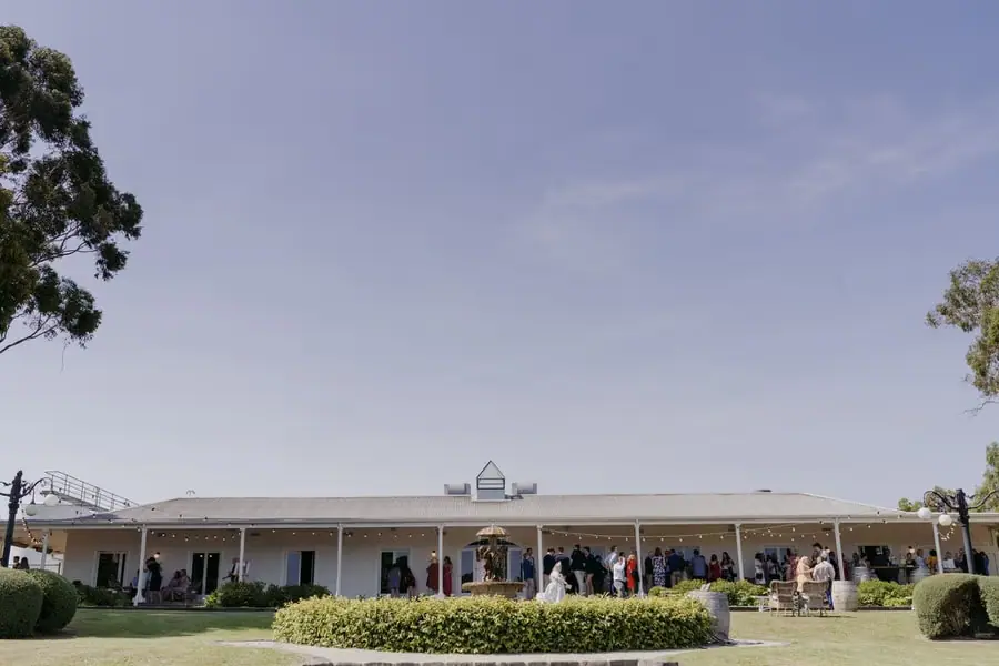 Guests gathering outside a long white building beneath a clear sky