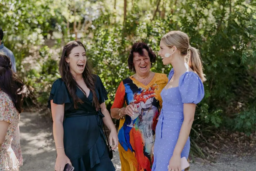 Three wedding guests laughing together in a leafy garden