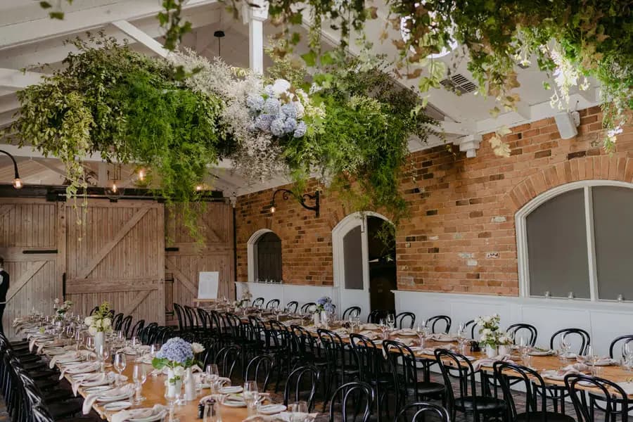 Reception room with long wooden tables beneath hanging flowers and greenery