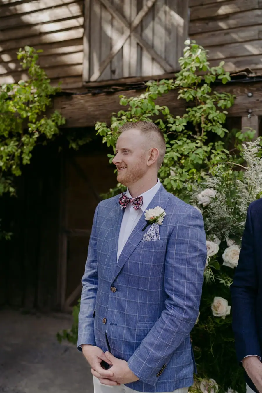 Groom smiling while waiting beside the ceremony building