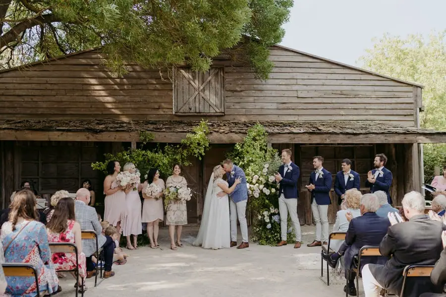 Wide view of the couple kissing as their wedding party and guests applaud