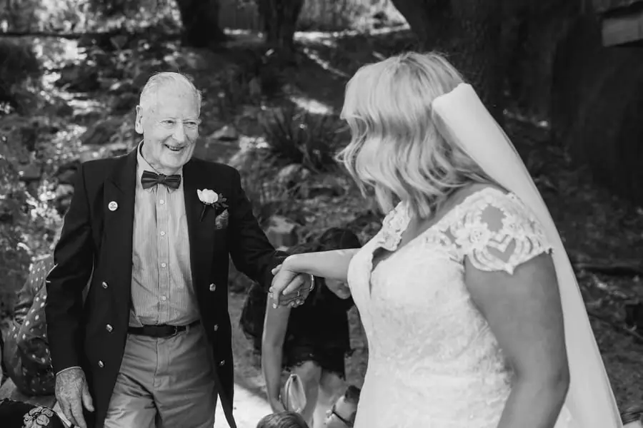 Black-and-white photograph of the bride smiling toward an older man after the ceremony
