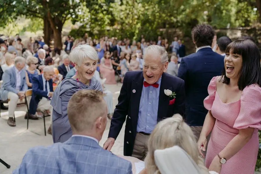 Bride and groom greeting laughing guests beside the ceremony benches