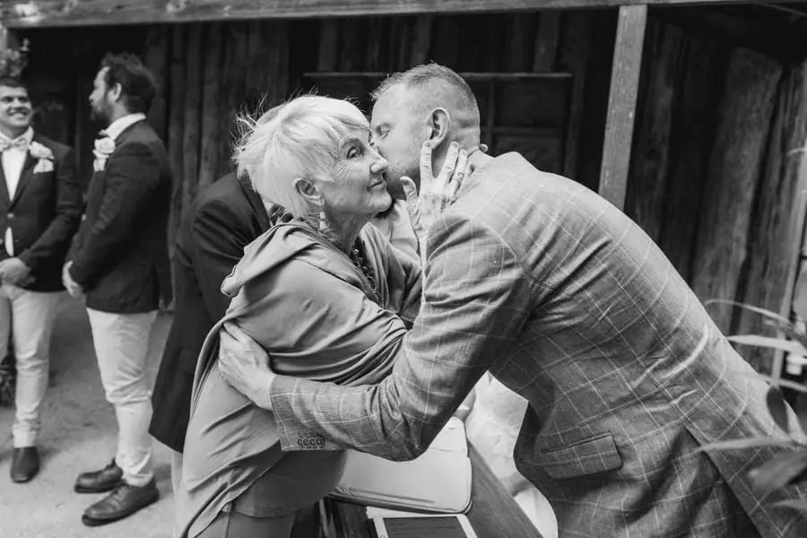 Black-and-white photograph of two older guests greeting one another with a kiss