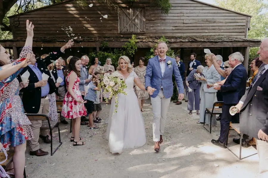 Guests throwing white petals over the couple outside the timber ceremony building