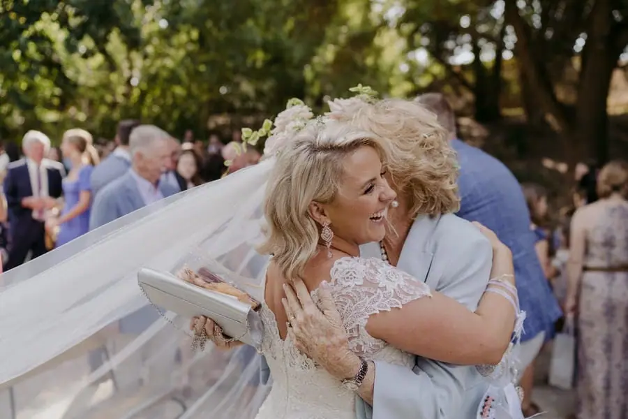 Bride hugging an older woman as her veil blows across the garden