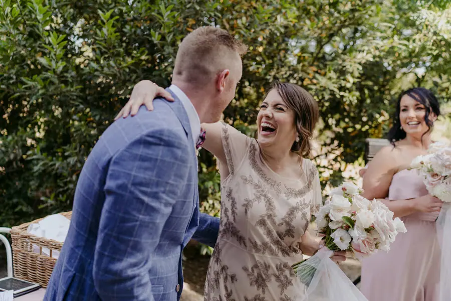Groom greeting a laughing woman holding a pale bouquet