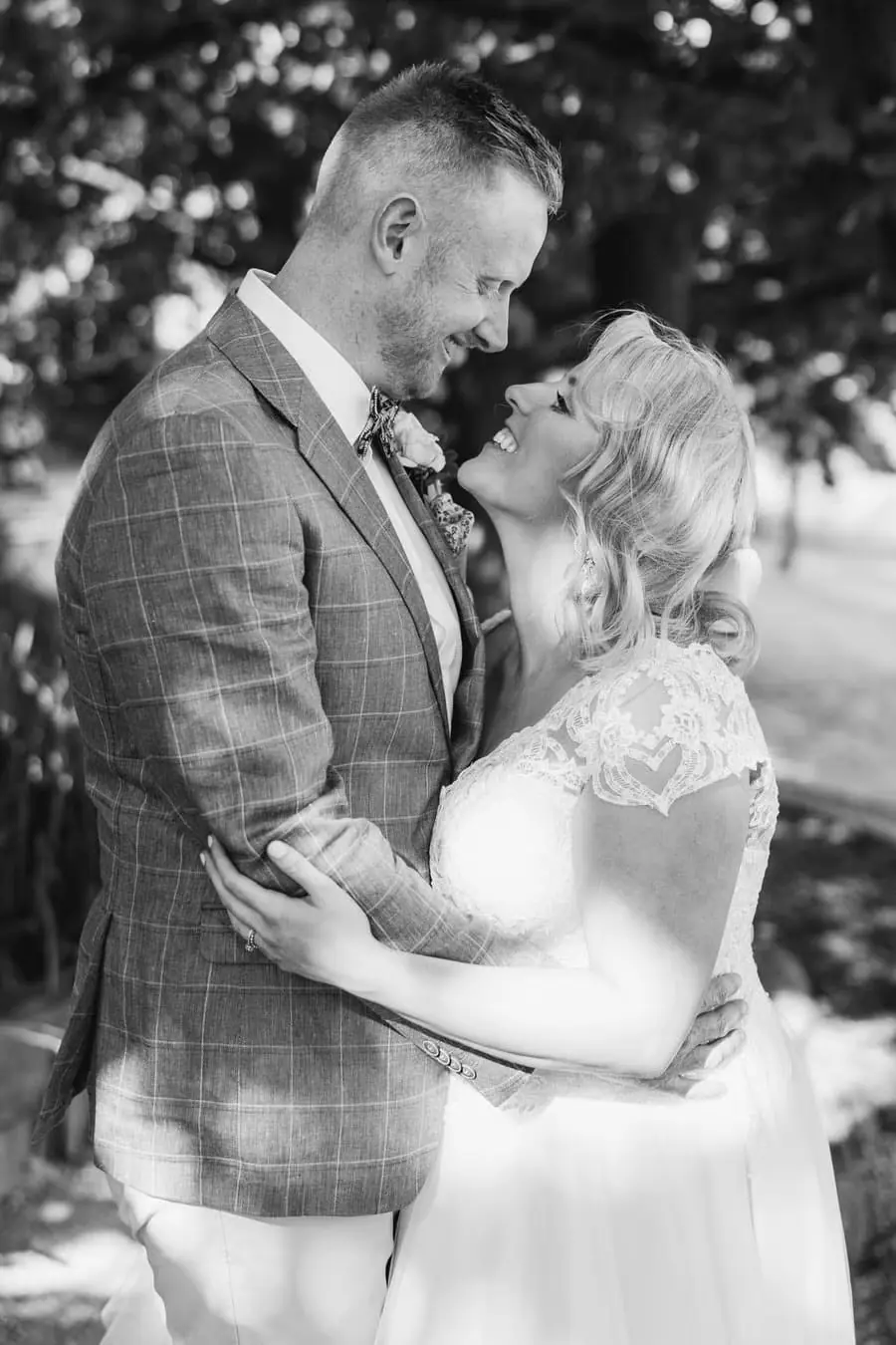 Black-and-white photograph of the bride and groom embracing beneath trees