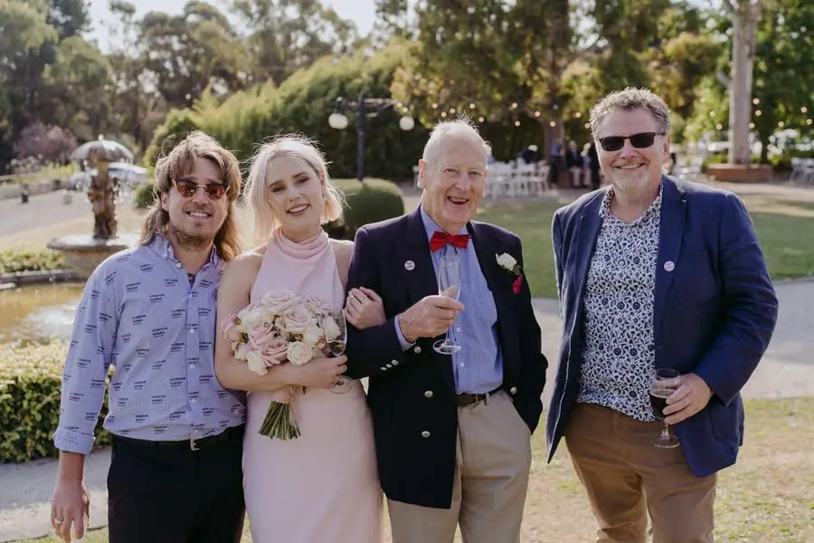 Four wedding guests posing together with drinks on a sunny lawn