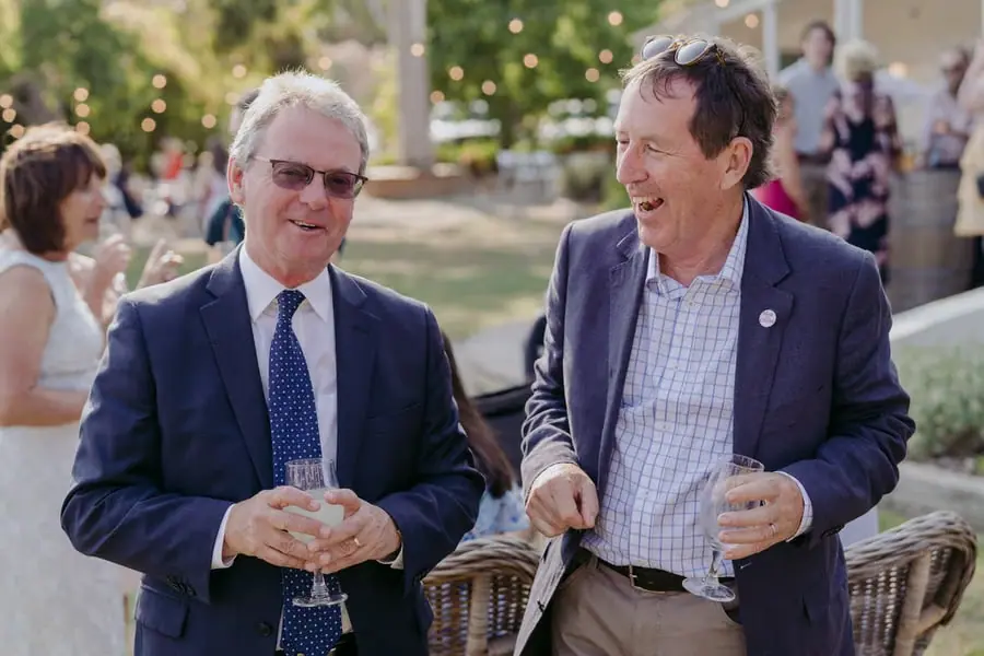 Two men laughing together while holding drinks outdoors