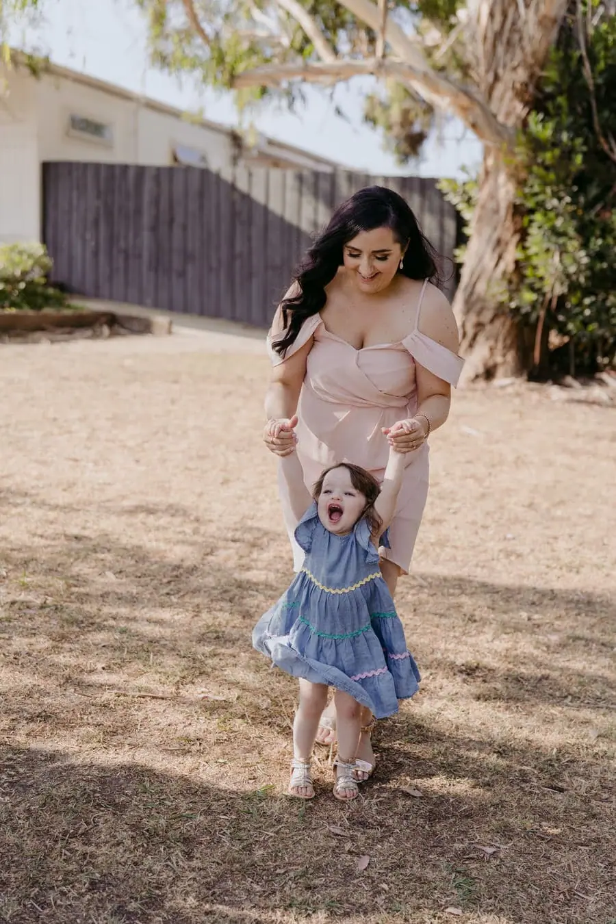 Woman helping a small child walk across dry grass