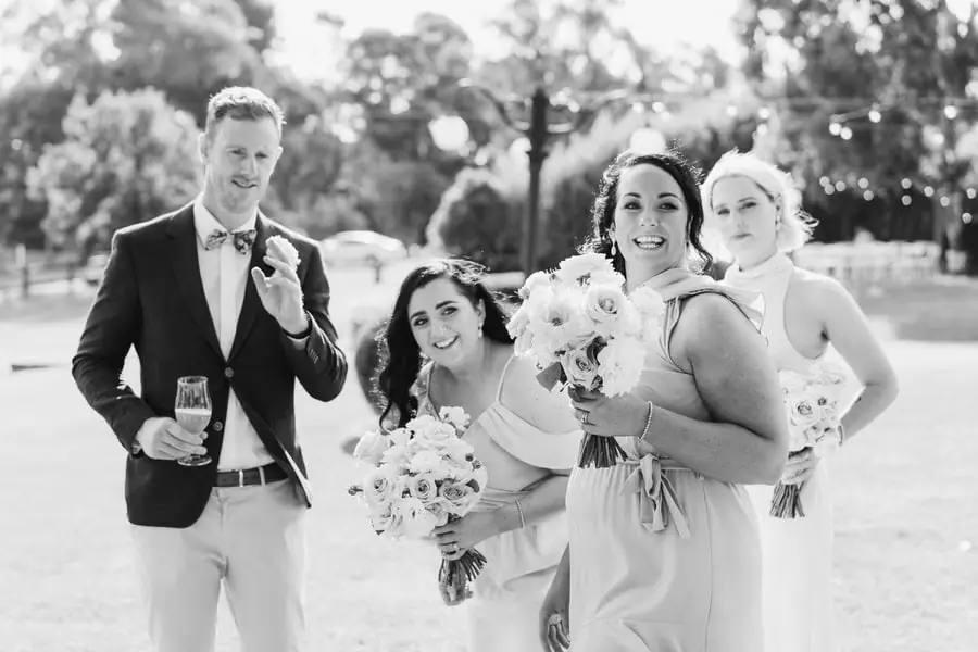Black-and-white photograph of four guests smiling with drinks and bouquets