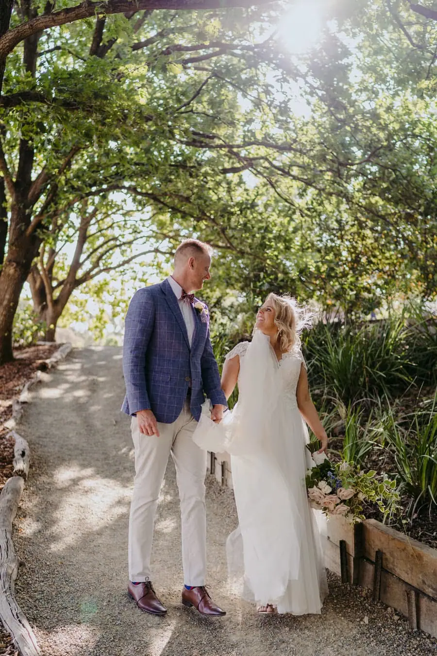 Bride and groom standing together on a tree-lined garden path