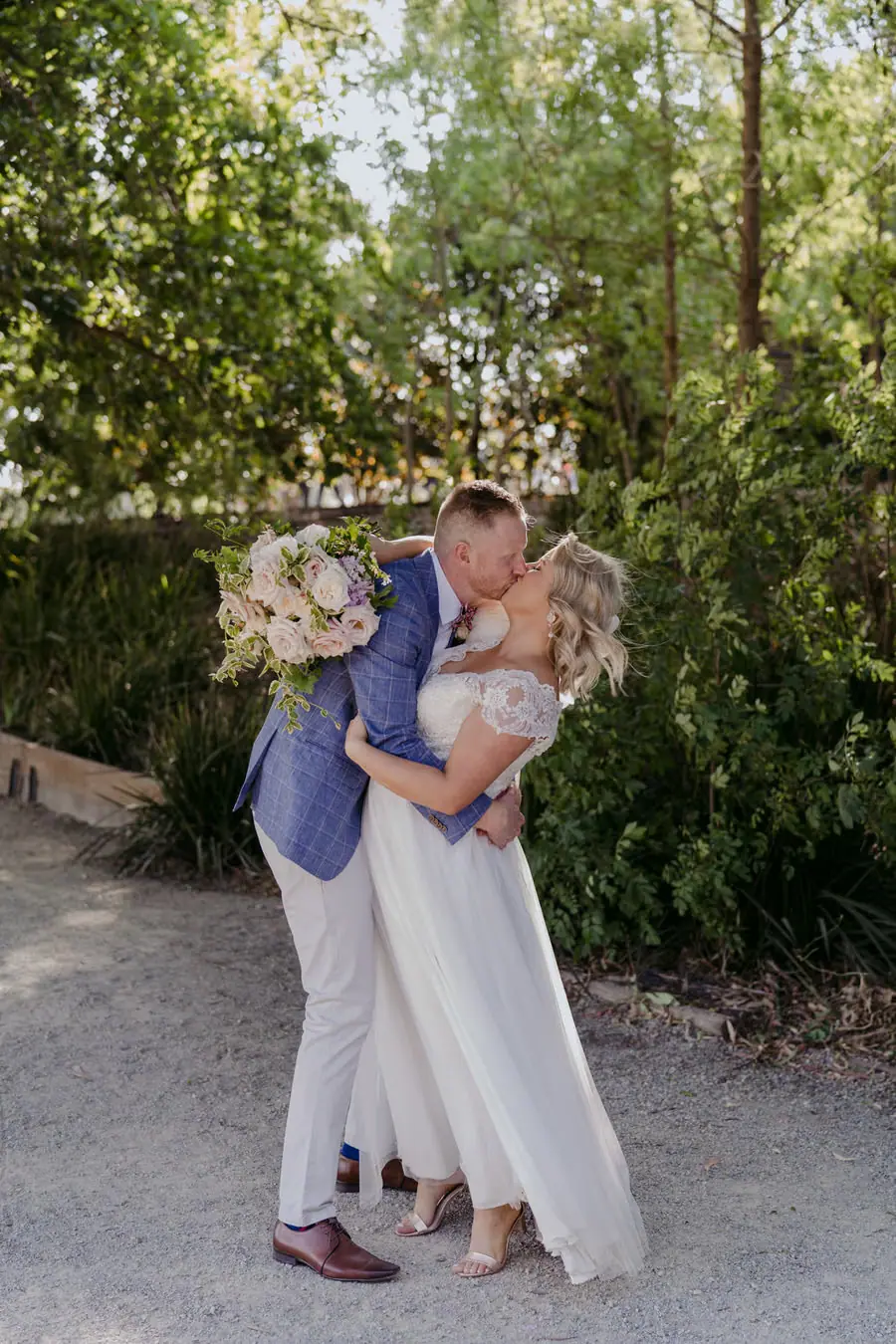 Bride and groom kissing beneath leafy trees