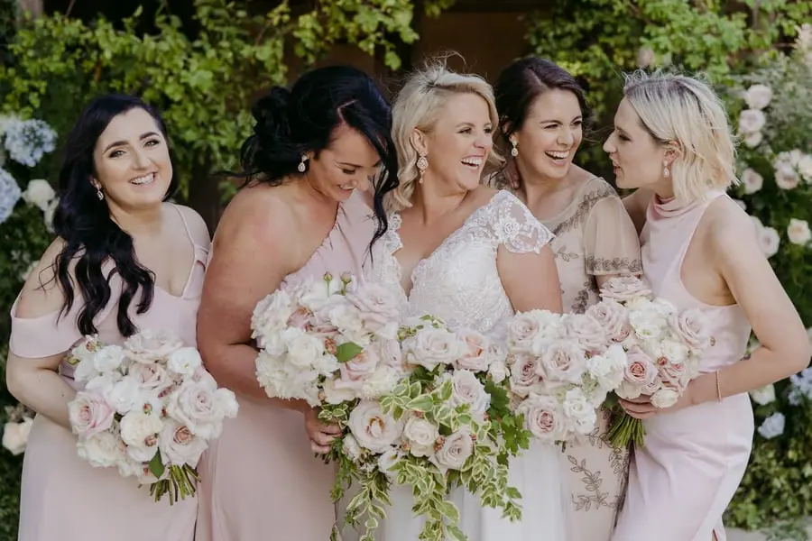 Bride and four bridesmaids leaning together with pale bouquets