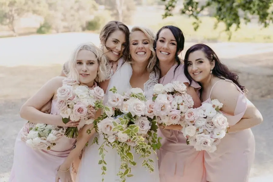 Bride and four friends smiling closely together with bouquets