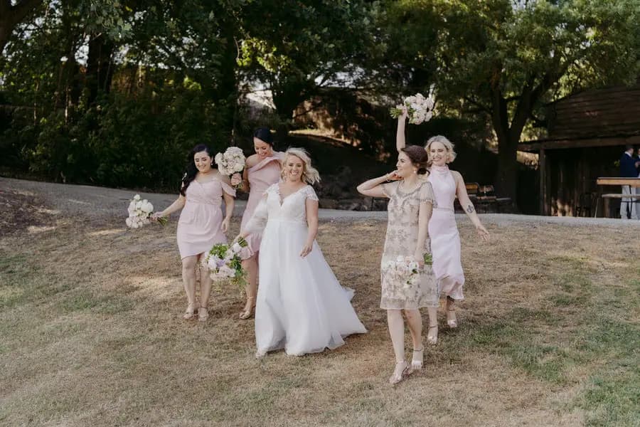 Bride and bridesmaids walking across a sunlit lawn