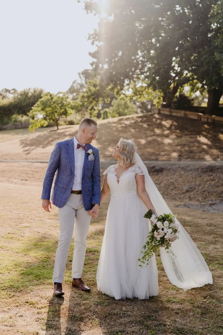 Bride and groom holding hands while walking beneath afternoon sunlight