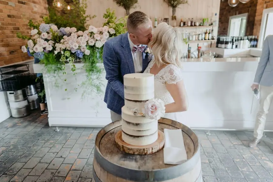 Bride and groom kissing beside a tiered wedding cake