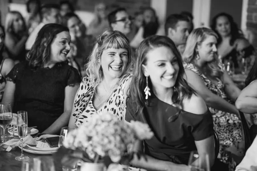 Black-and-white photograph of seated guests laughing at a reception table