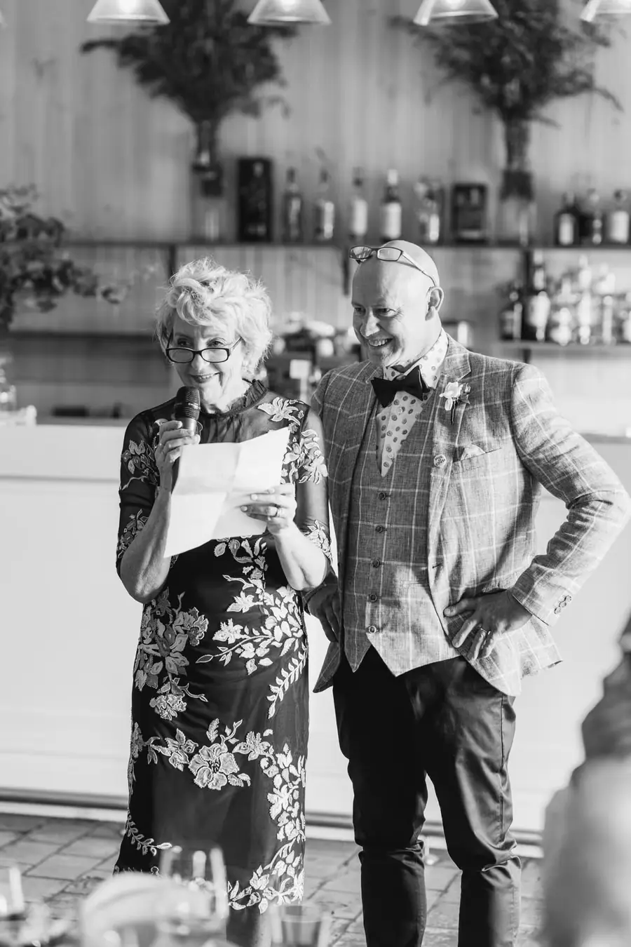 Black-and-white photograph of two older guests standing together with drinks