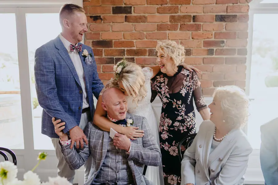 Bride embracing a seated older man as guests smile around them