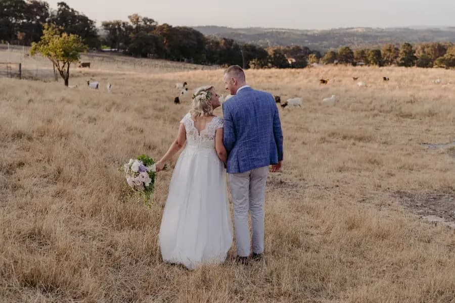 Bride and groom standing in a dry grassy field with grazing animals behind them