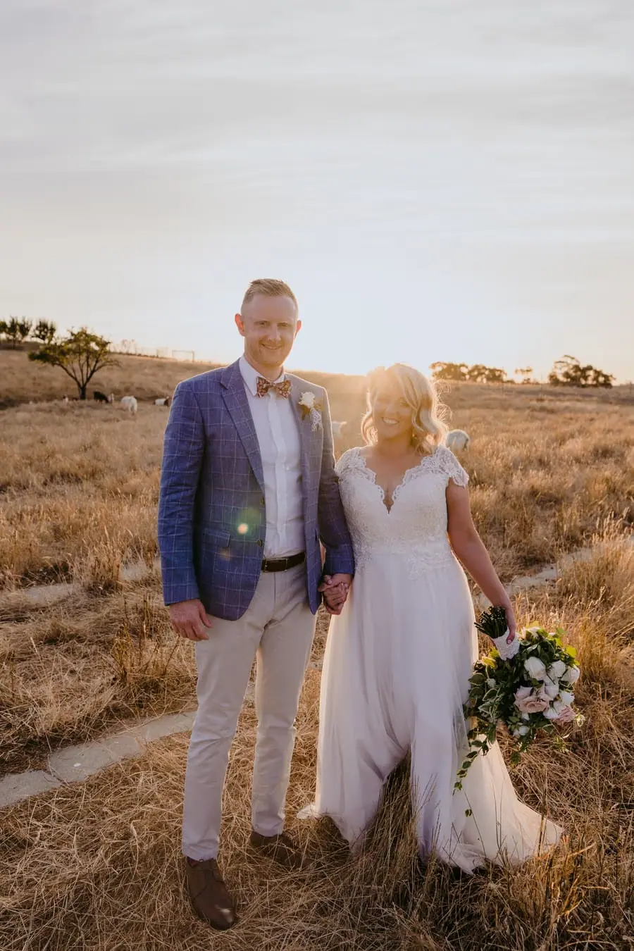 Bride and groom standing together beside a field path at sunset
