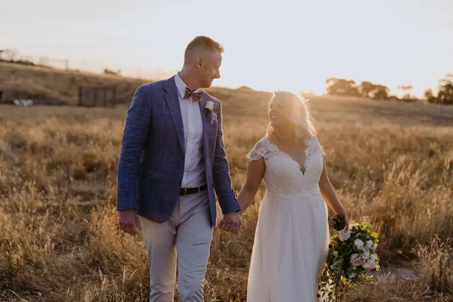 Bride and groom smiling toward one another while holding hands at sunset