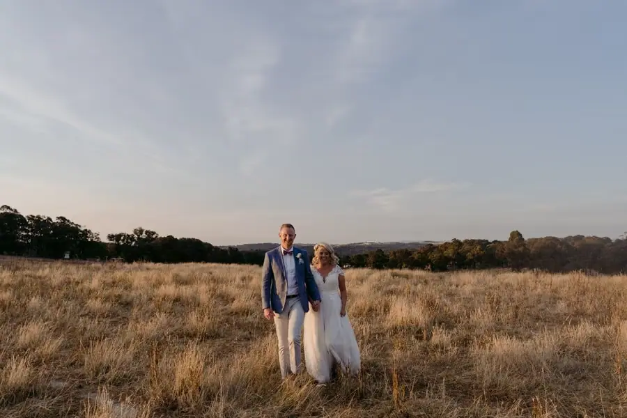 Wide view of the couple standing in a field beneath an evening sky