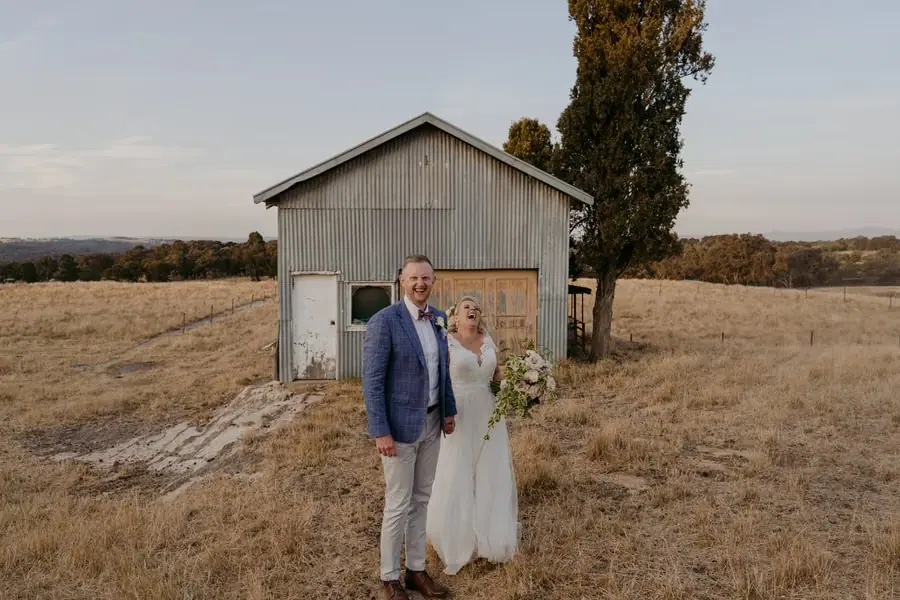 Bride and groom standing in front of a small weathered farm shed