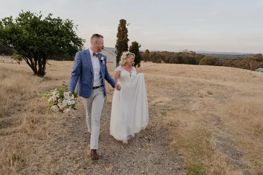 Bride and groom walking hand in hand along a grassy field path
