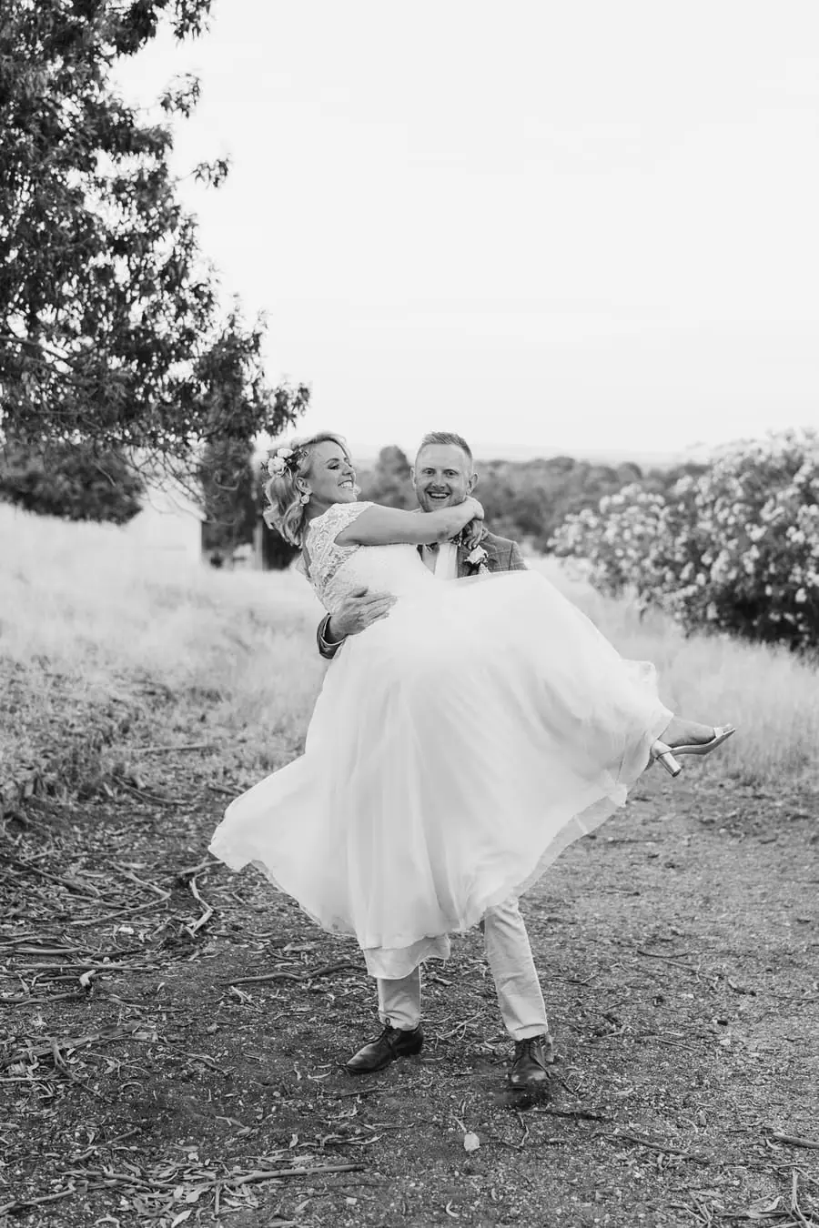 Black-and-white photograph of the groom carrying the laughing bride in his arms
