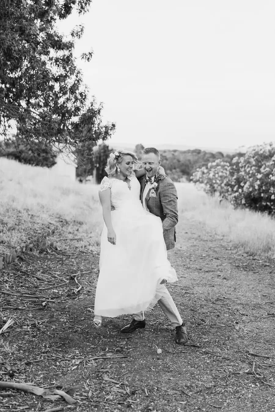 Black-and-white photograph of the groom lifting the smiling bride beside a field path