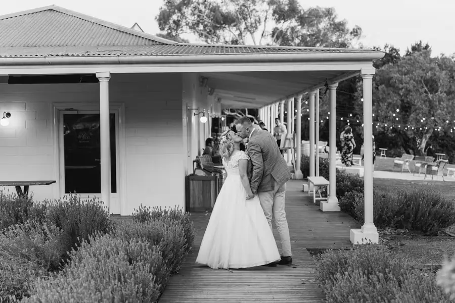 Black-and-white photograph of the bride and groom kissing beside a verandah