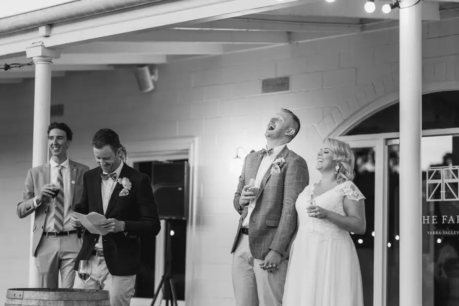 Black-and-white photograph of a man speaking into a microphone beside the bride and groom