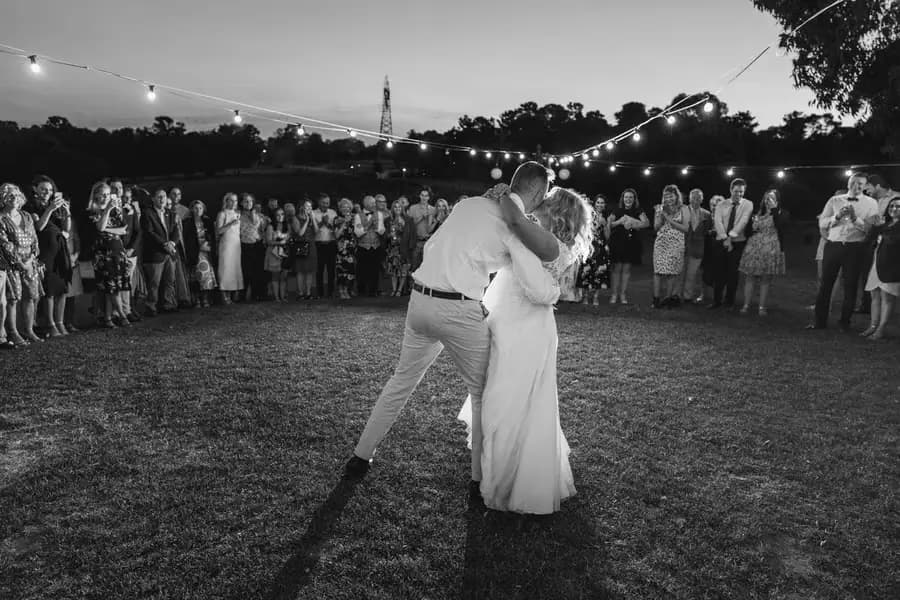 Black-and-white photograph of the groom dipping the bride into a kiss on the lawn