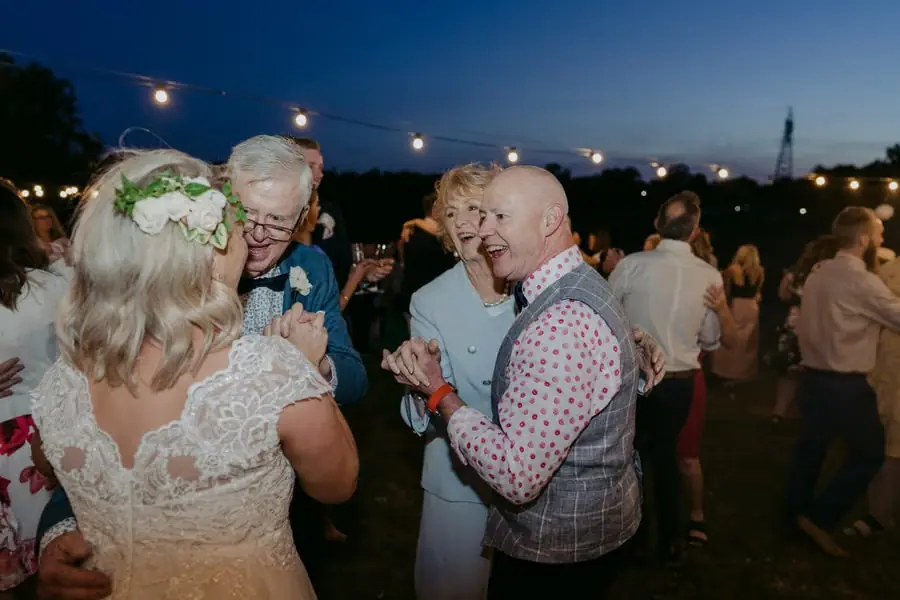 Bride dancing with older guests beneath glowing festoon lights