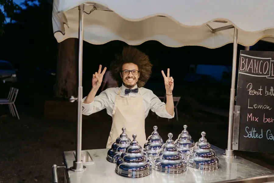 Gelato vendor smiling and raising both hands behind a serving cart